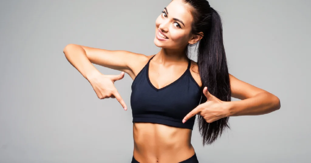 Woman smiling and pointing to toned abs, representing results from Non-Invasive Laser Lipo in Houston, TX.