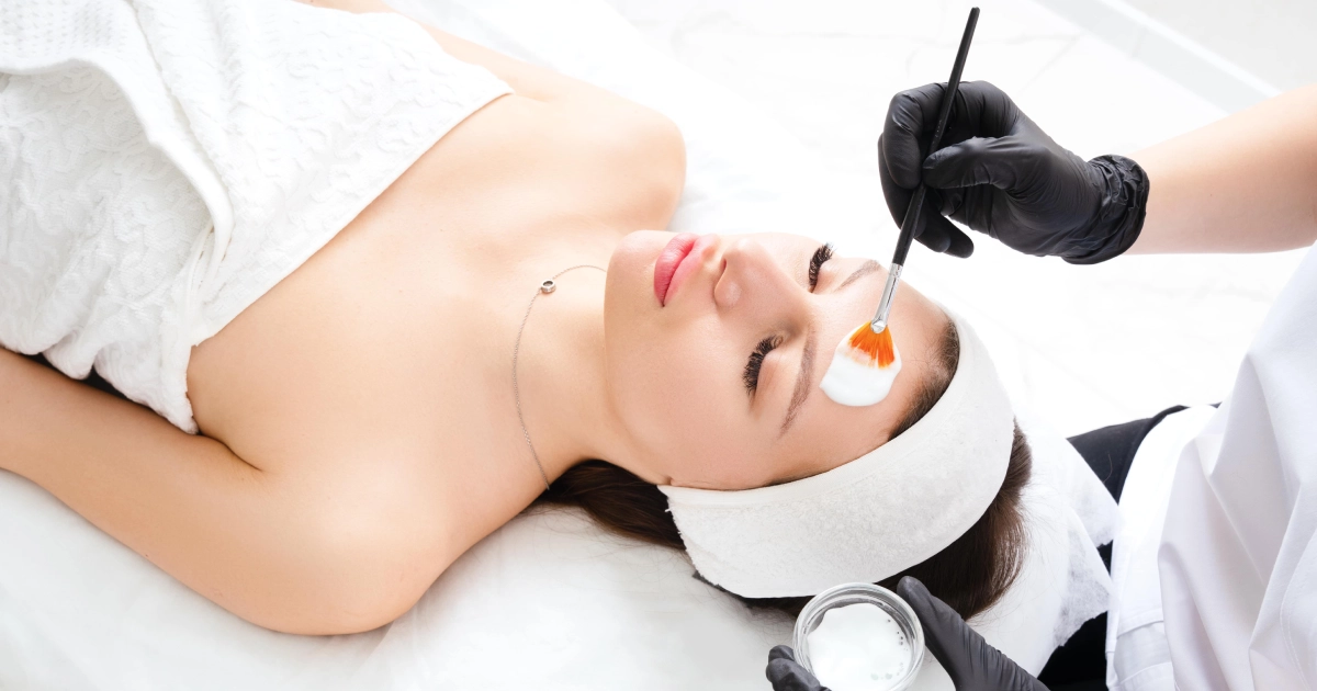 Woman receiving a facial treatment with a white mask or peel applied by a professional with a brush, suggesting a VI Peel in Houston, TX.