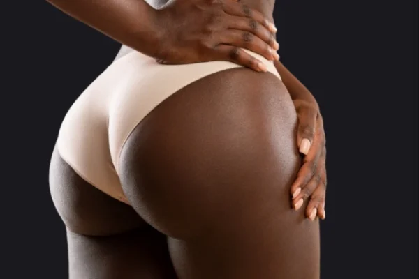 A woman in nude-toned underwear poses with one hand on her hip, highlighting her smooth and sculpted curves against a dark background. The image emphasizes body contouring results and confident posture.