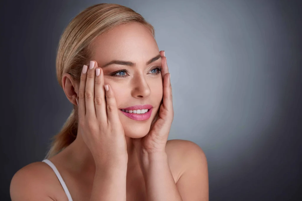 Woman with glowing skin gently touching her face and smiling after a facial rejuvenation treatment at The Better Body Shop in Houston, TX