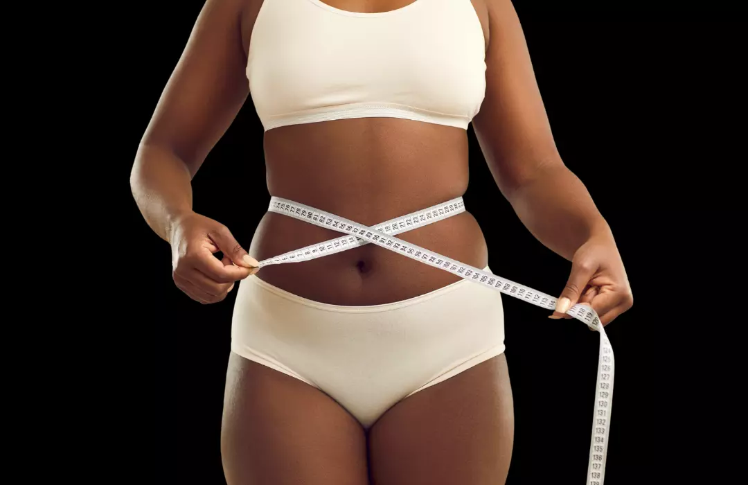Woman in workout clothes measures her waist, showcasing her medical weight loss program results.